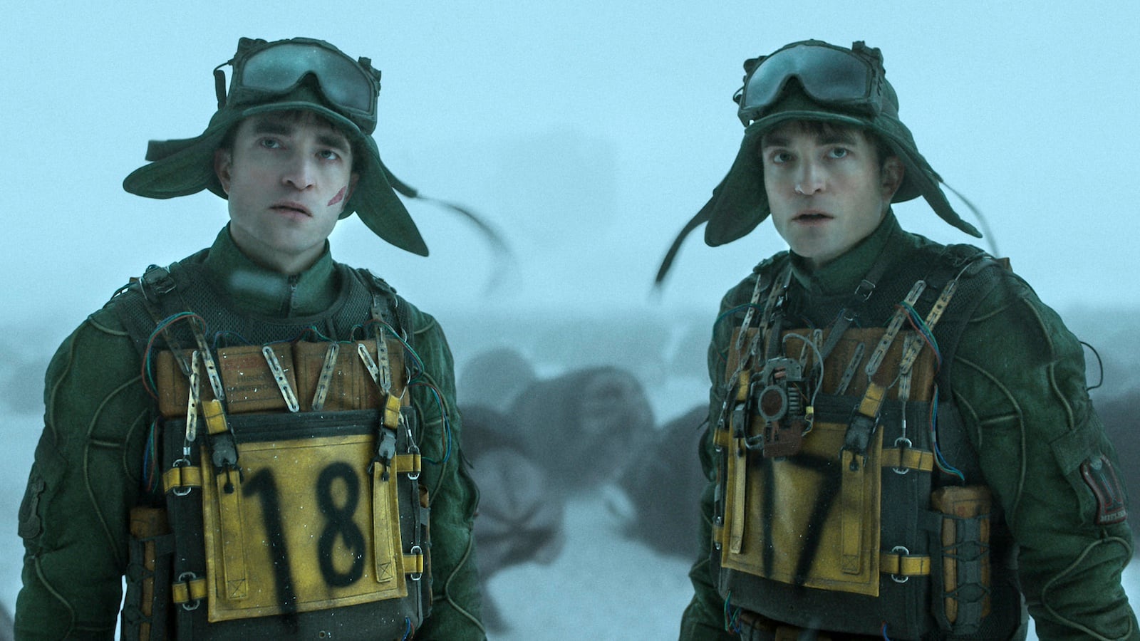 Film still of two men that look identical wearing uniforms and googles and the numbers 18 and 17 spray painted on them respectively