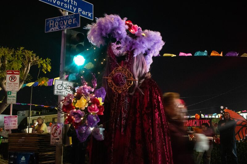 An attendee dressed as La Catrina watches performances from the back of the crowd.