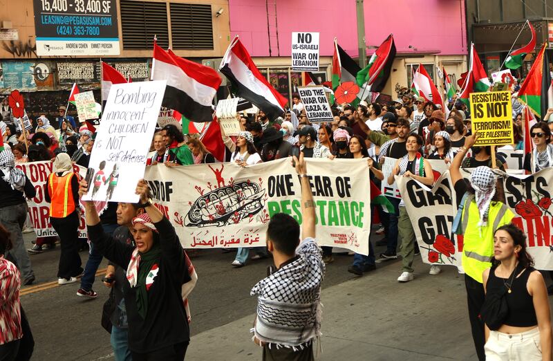 Pro-Palestinian protestors donning keffiyehs and holding signs and flags march through the street in downtown Los Angeles.