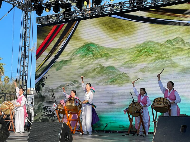 Photo of a group of women on a stage in red and pink beating drums