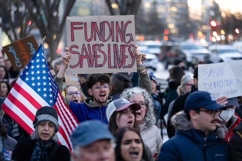 Picture of a man holding a sign that says "Funding saves lives"