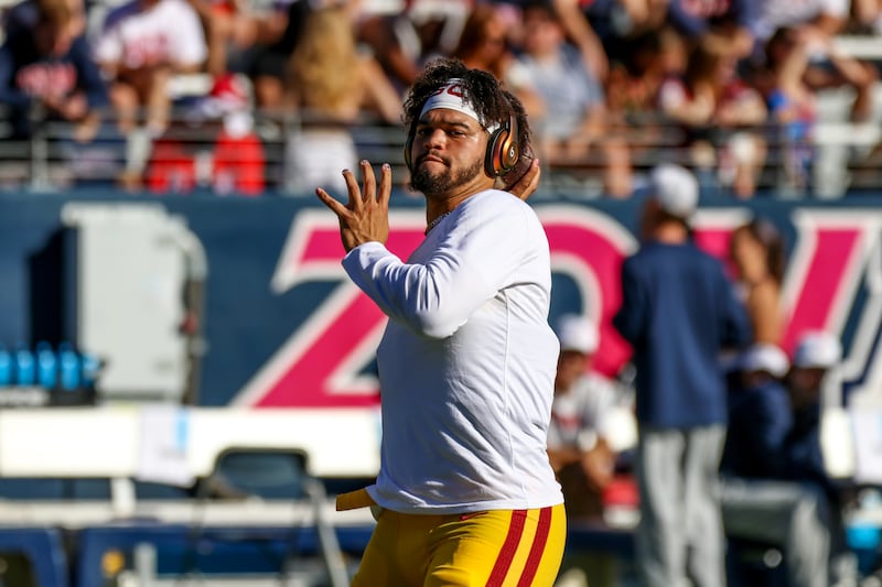 Williams looks downfield with arm cocked back as if to throw a football. He wears a white long-sleeved shirt with gold and cardinal football pants.