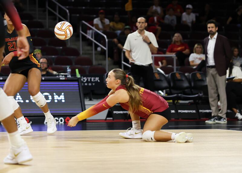 Taylor Deckert crouches down low on a court to the ground to dig a volleyball. She wears a cardinal volleyball uniform with gold accents.