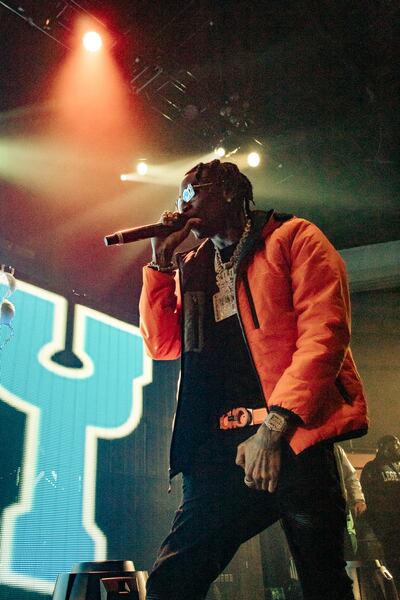 A photo of Soulja Boy in an orange puffer coat singing into the microphone on stage.
