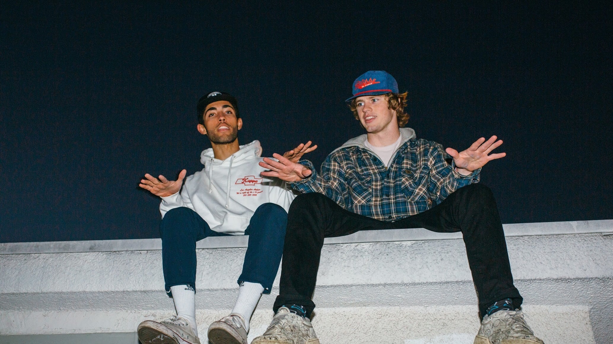 A photo of Marius Bell, 20, and Garrett Murphy, 21, sitting on the edge of a wall side by side.