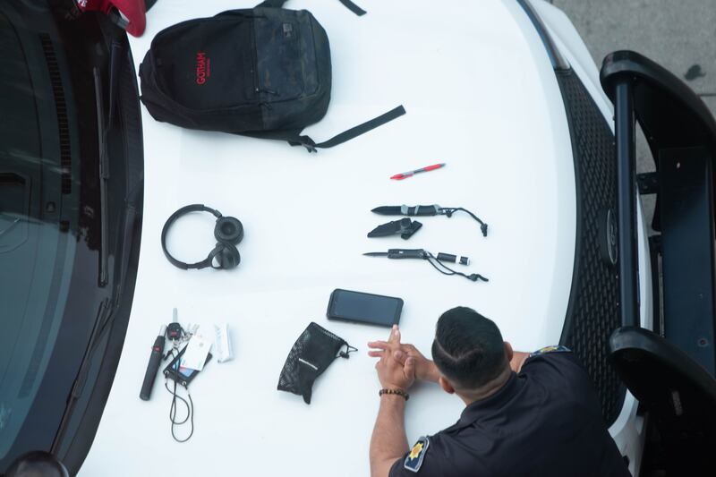 A photo of a Gotham Hollywood backpack, two knives and sheaths, a visa card, headphones, phone and a red pen are among the belongings sitting on the hood of a DPS police vehicle.