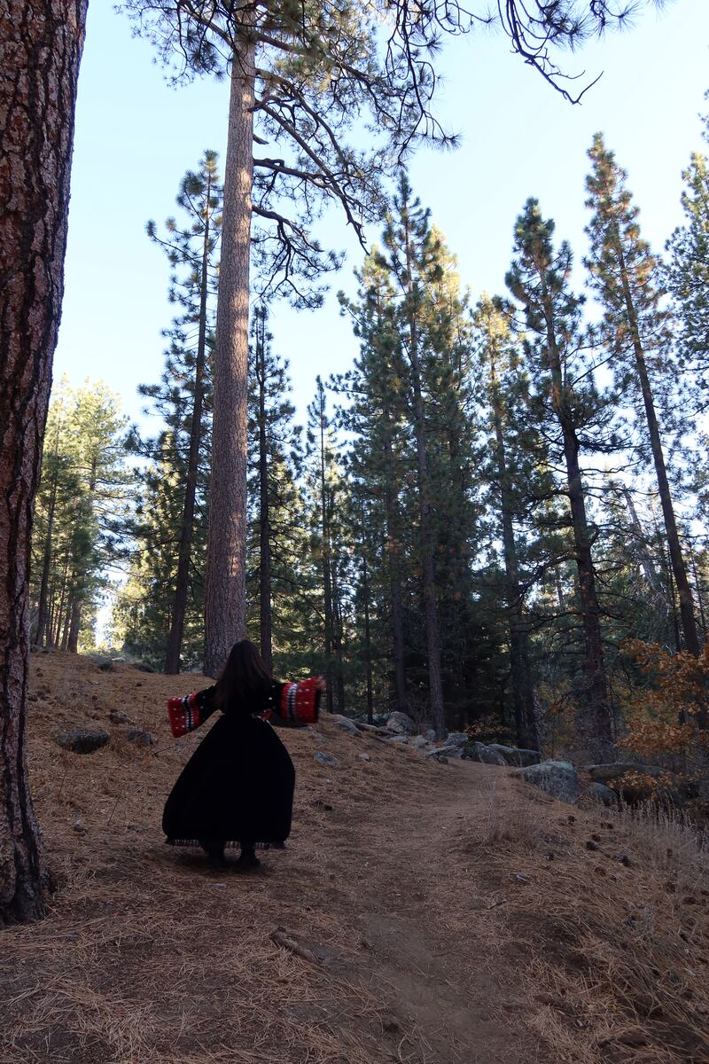 Girl spinning in a black velvet Afghan dress with trees surrounding her.