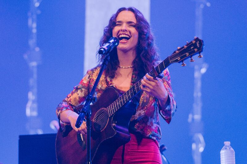 A photo of Raine singing into a microphone and playing the guitar