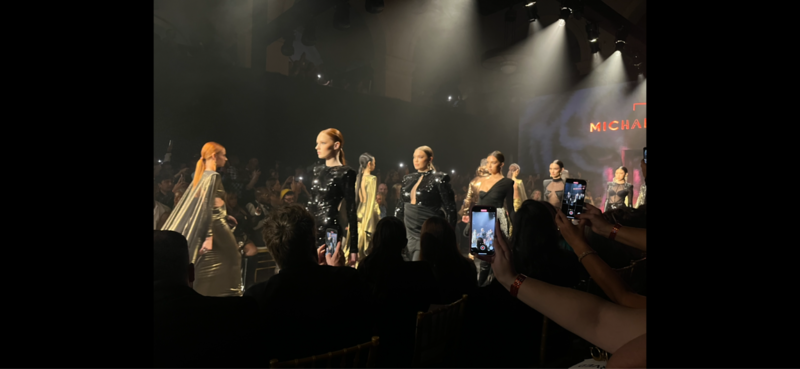 A large group of models walk down a catwalk in several different styles of outfits.