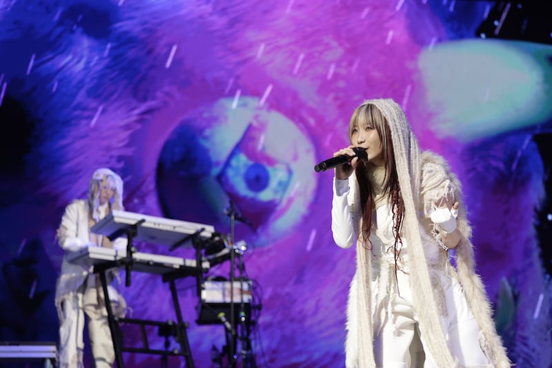 Photo of a woman in white singing on stage in front of a man on a synthesizer