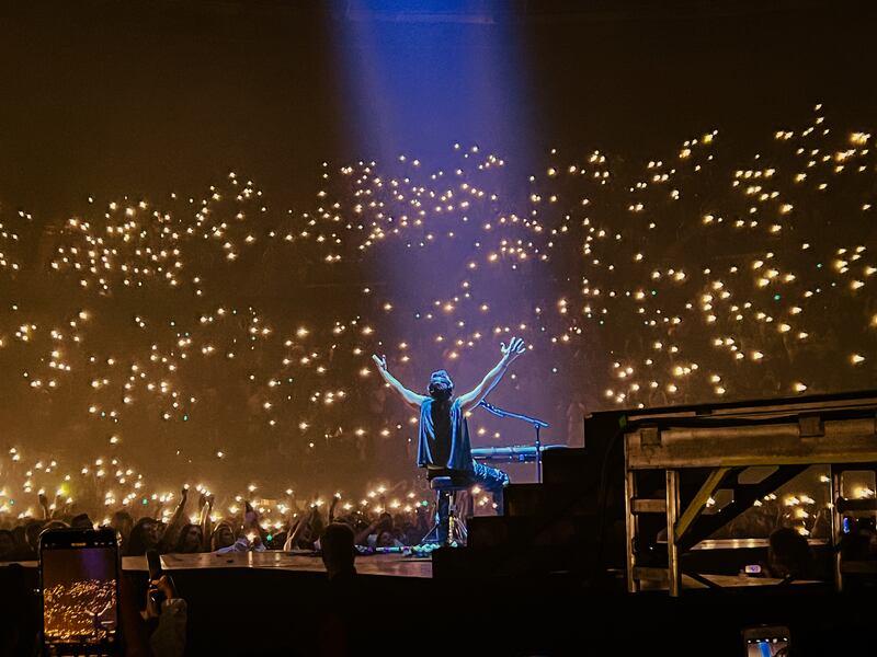 A singer throws his hands up behind a piano on stage to engage with the crowd.