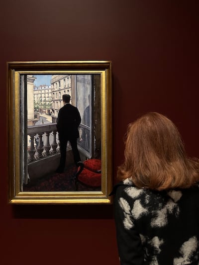 A woman in a black and white flower jacket looks at the painting.