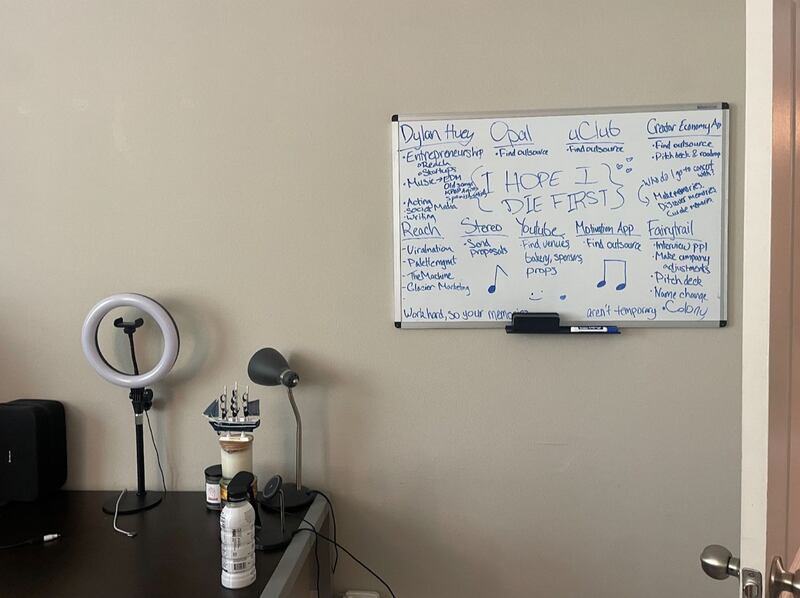 Against a beige wall, a white board is covered in scribles in blue marker. The board lists different social media sites and Huey's goals.