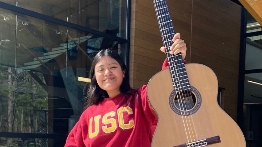 Wearing her read USC crew neck sweater, second-year classical guitar major, Daniela Santiago holds up her classical guitar proudly.