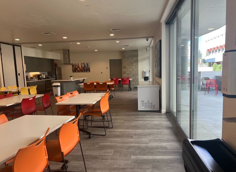 A clean room with tables that seat four people, with orange and red chairs.