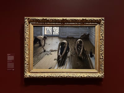 The painting is against a red wall and in a gold frame.