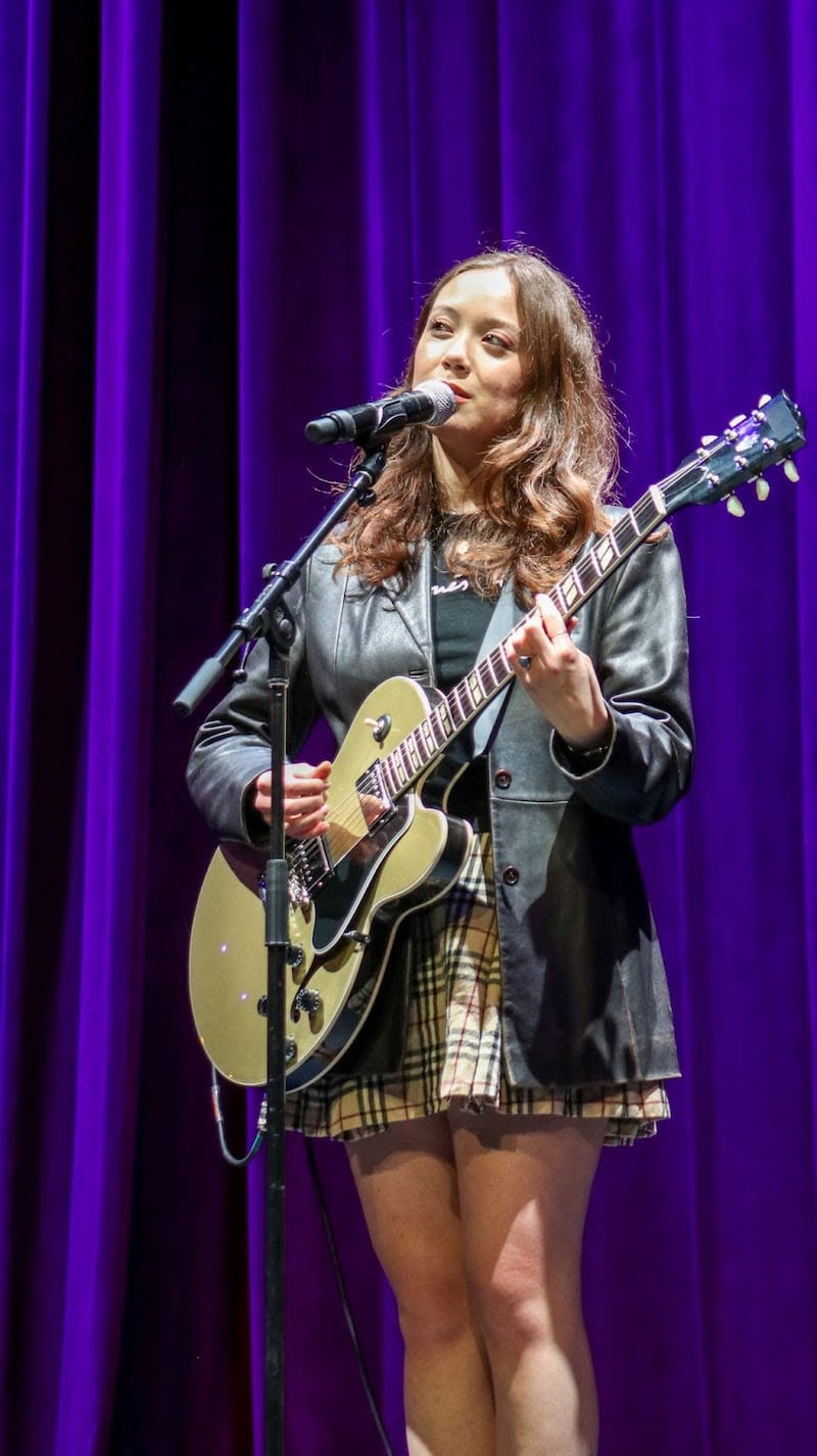 Laufey sings into a microphone while holding a brown electric guitar