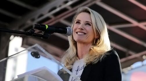 A blonde woman smiles at a podium