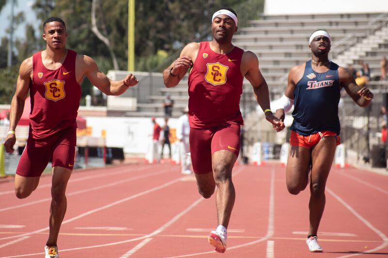 Two USC runners and a Cal State Fullerton runner cross a finish line.