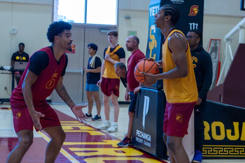 Easter II (right) stands in profile holding a basketball; it looks like he is trying to inbound the ball around teammate Rodney Rice (left), who is in a defensive stance. Easter II wears a gold practice jersey, while Rice wears a cardinal practice jersey.