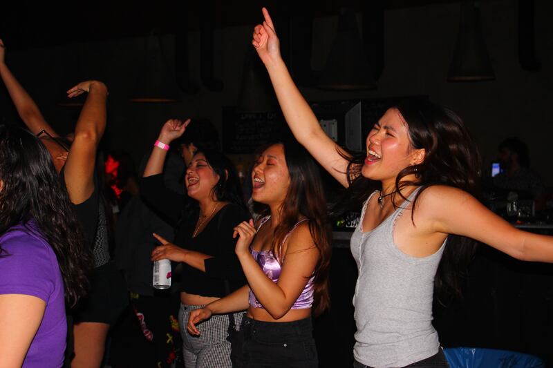Three fans sing along with their arms up in the air.