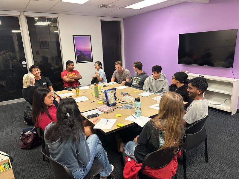 Students sit around a table with pen and paper in front of them.