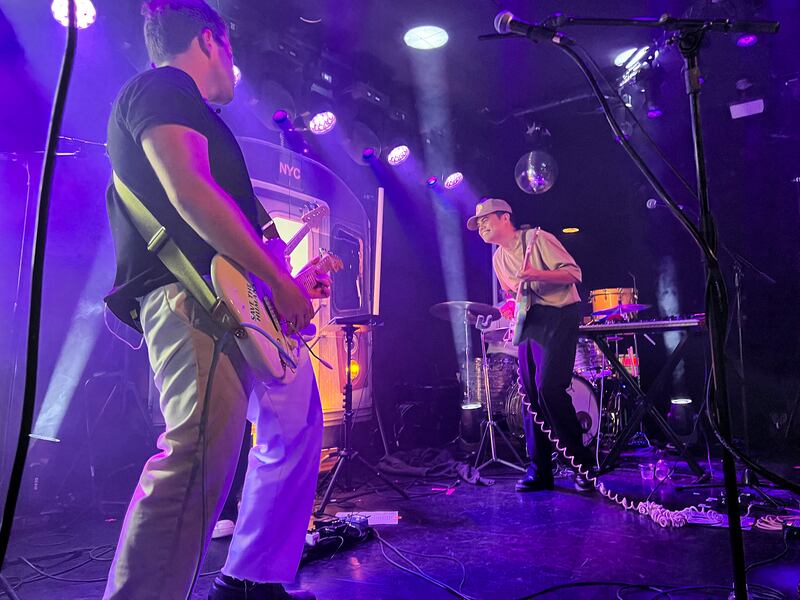 Photo of a man with a guitar looking at another man on stage with a guitar