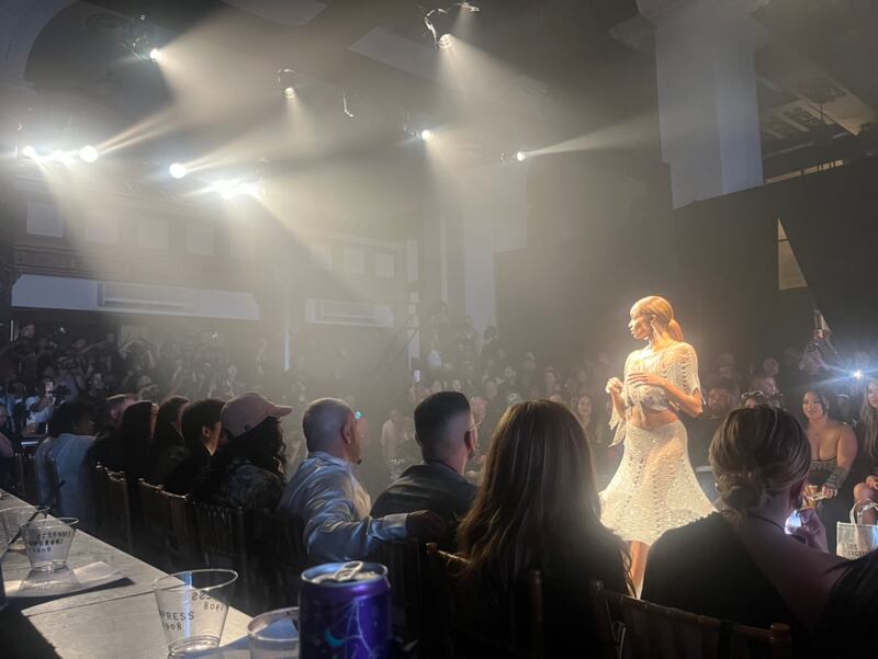 A model in a white dress looks down the runway as viewers look on.
