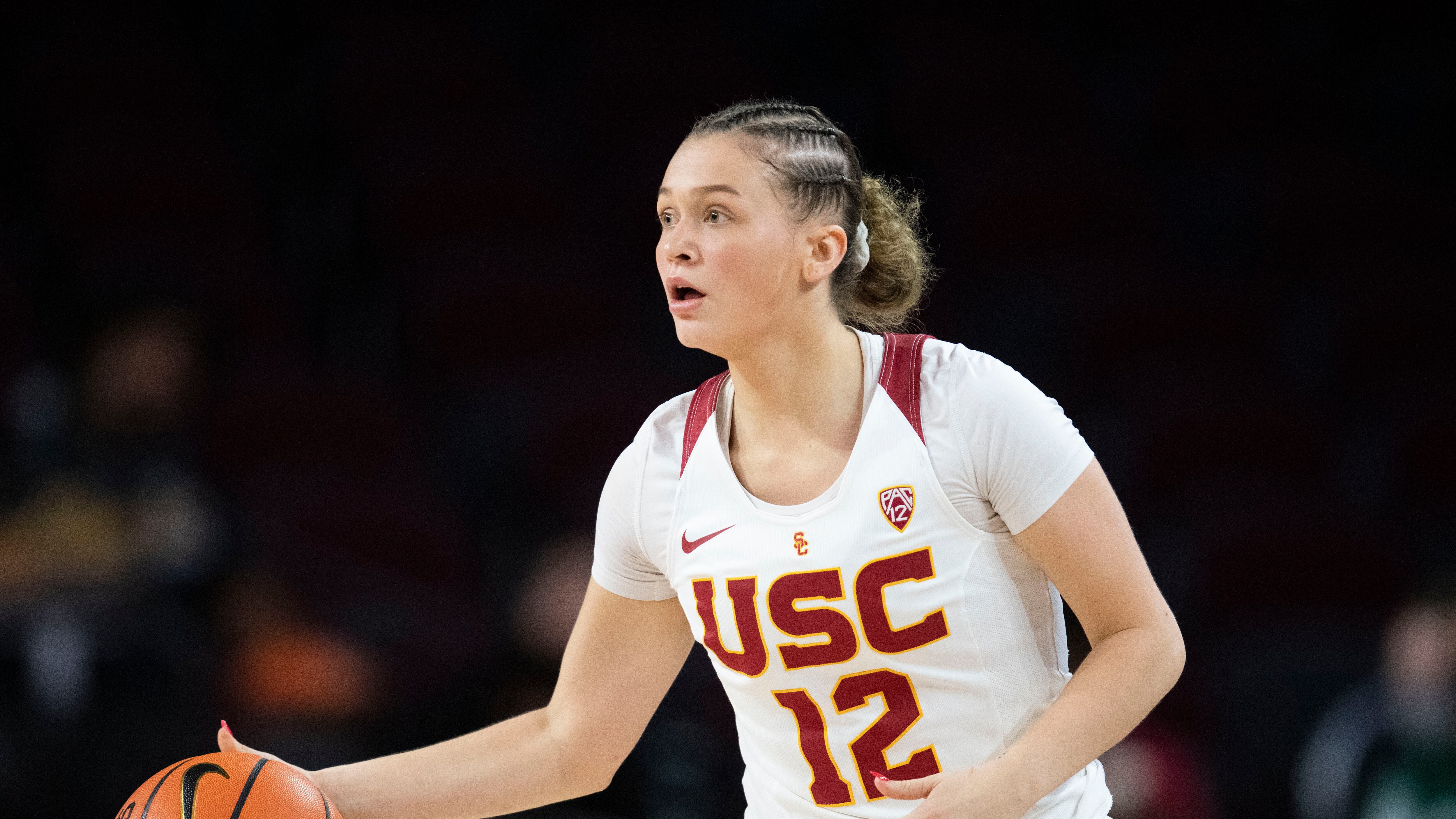 A photo of USC freshman guard Bella Perkins in a white jersey dribbling a basketball with her right hand and looking up the court.