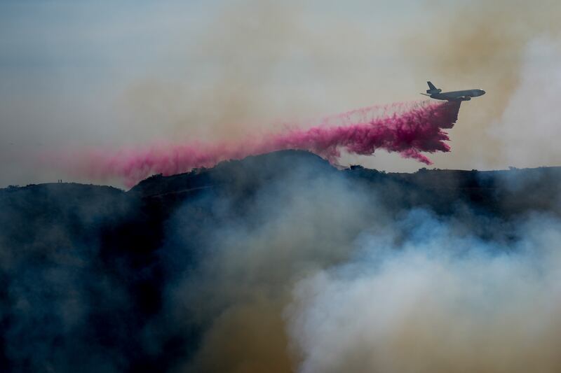 A plane drops hot pink powder over a smoking hill.