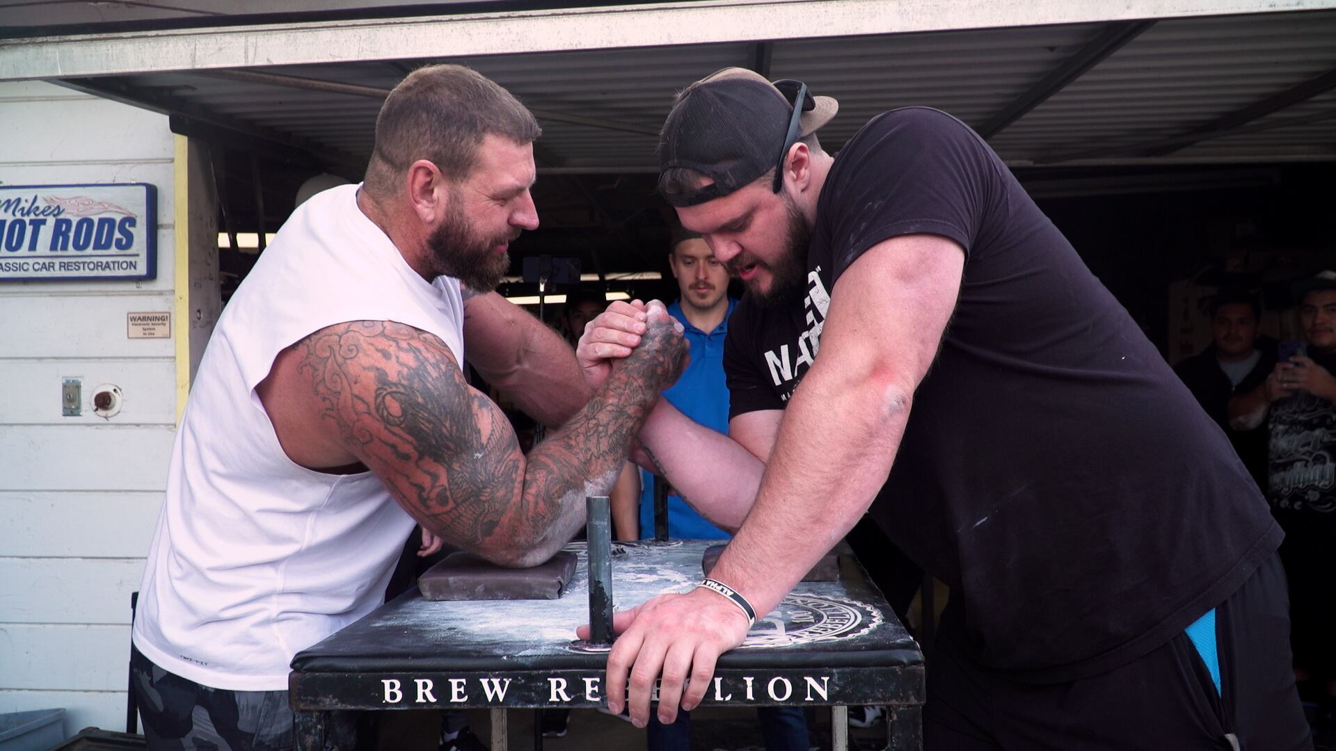 Two men arm wrestle over a table.
