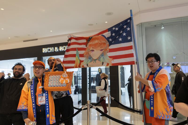 Photo of a group of people wearing orange outfits holding an American flag with an anime girl on it
