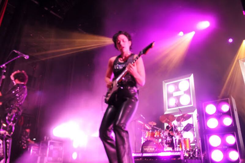 Josette Maskin wears all black while playing the electric guitar under purple lights