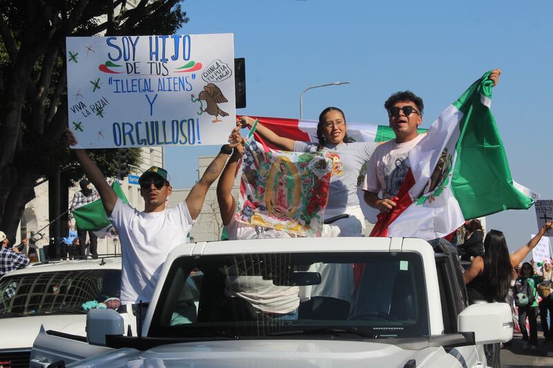 Photo of people in a car holding a sign and a Mexican flag.