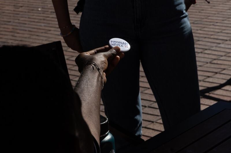 A hand holds out a Hannah-Nivea 22 button to another person.