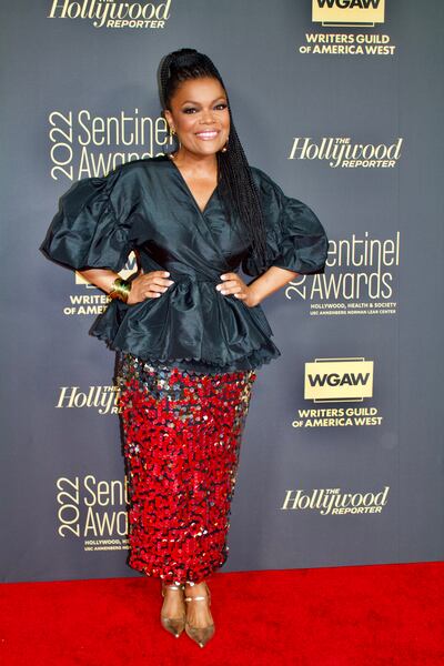 A photo of Brown in a black top and sequin skirt smiling and posing on the red carpet.