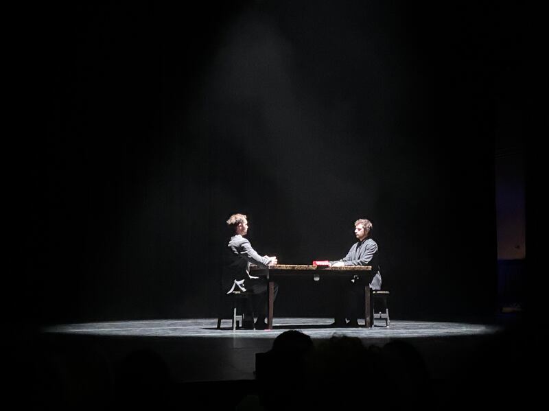 The dancers of JA Collective sit on opposite sides of the table, staring at each other.