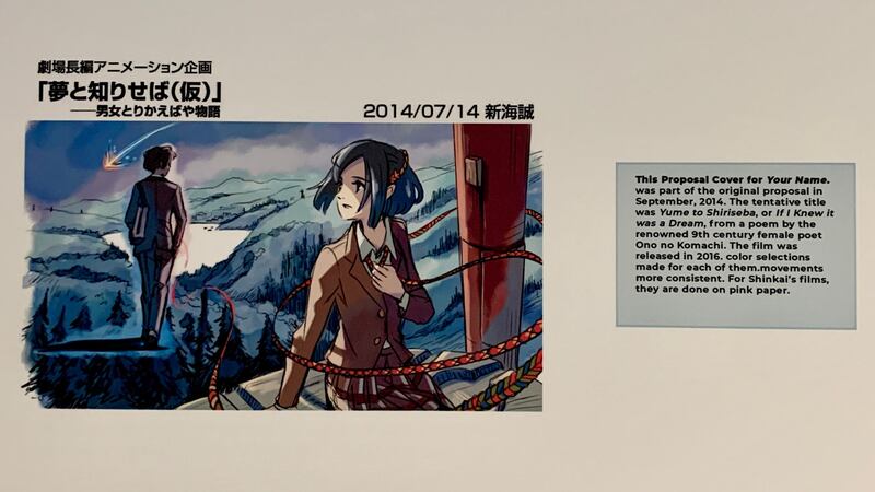 A photo of the exhibit of Makoto Shinkai’s past directorial work featuring a drawing from a film and a text block about the drawing.