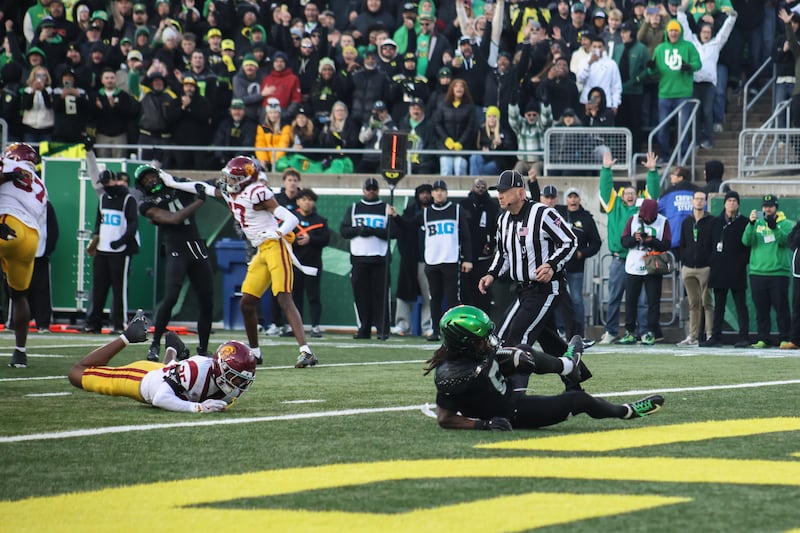 An Oregon football player slides into the endzone at Autzen Stadium; a referee and two USC defenders can be seen in the background.
