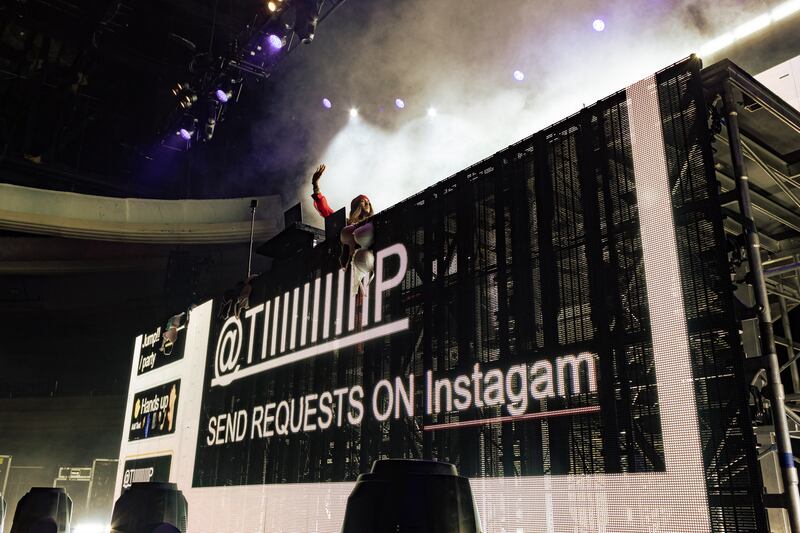 A photo of the stage at the concert with DJ Tiiiiiiiiiip's set up, which includes a black and white screen with his Instagram handle and the words "Send requests on Instagram." There is a bra hanging on top of the sign, likely thrown on the stage by a fan.