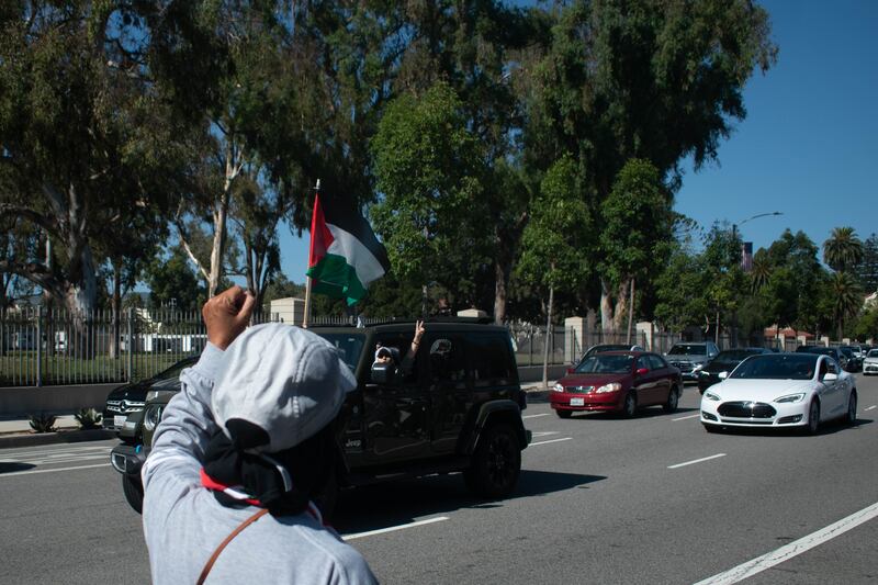 A car with a Palestinian Flag drives by the protest and puts up a peace sign in solidarity.