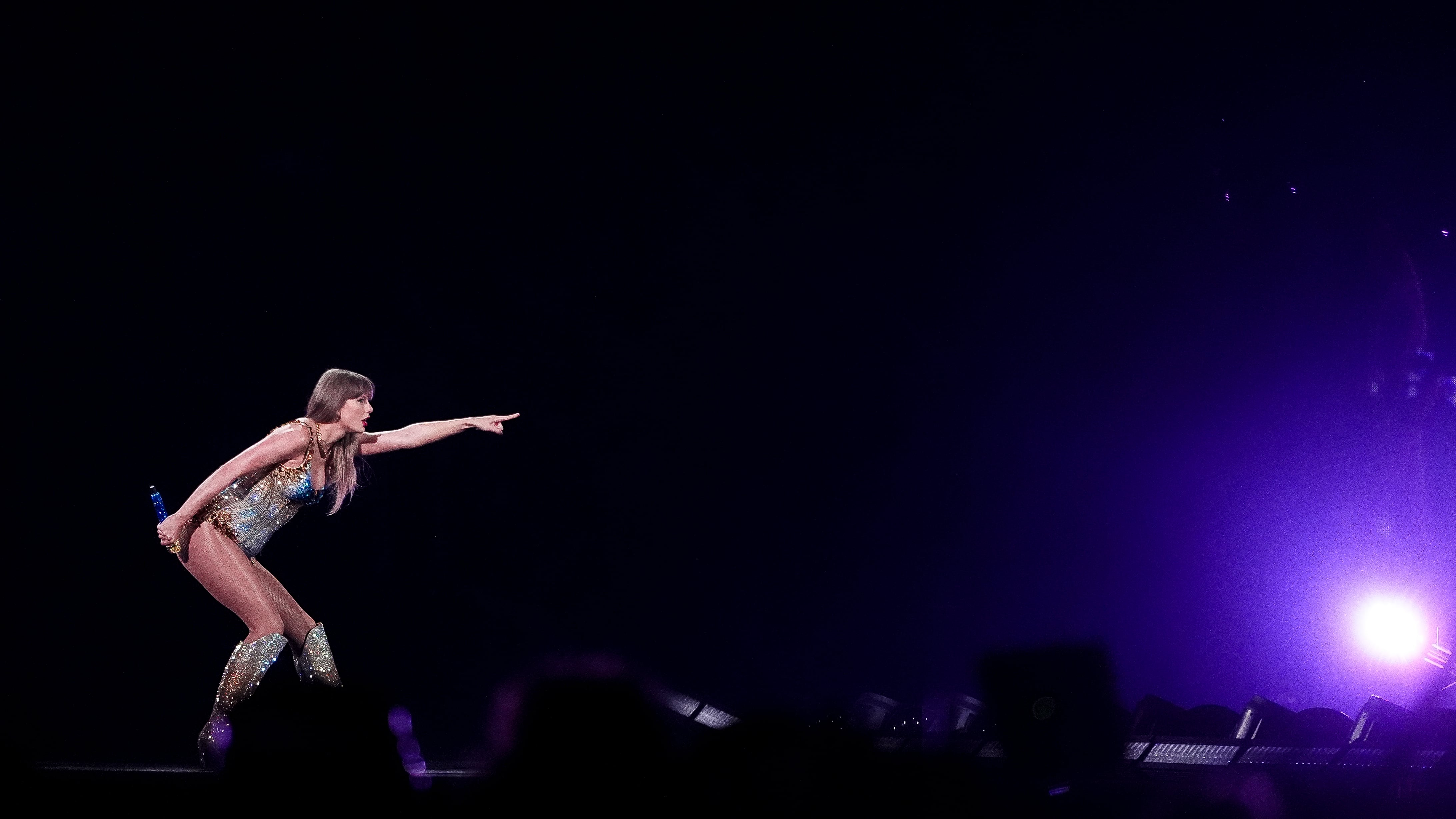 Taylor Swift, a blonde white woman, points to the right while performing on stage.