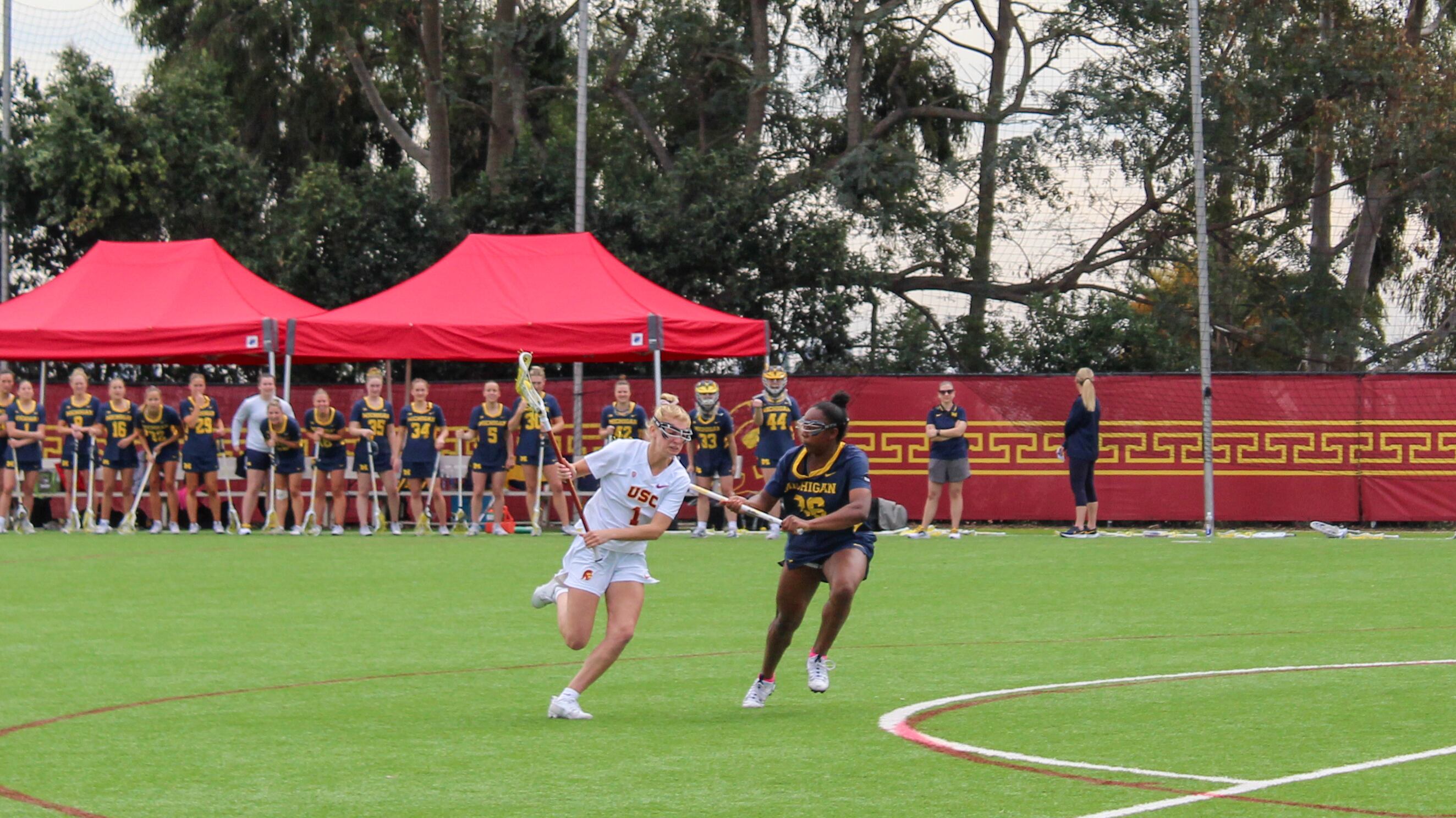 Redshirt junior attacker Isabelle Vitale, wearing the number 1 jersey in white, tries to outpace a Michigan defender wearing a navy jersey with maize yellow trim.