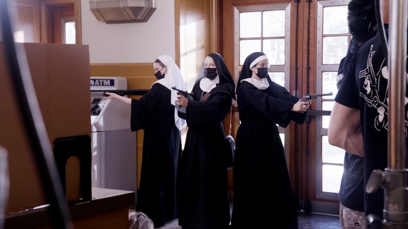 The three nuns point their guns as they enter the bank.