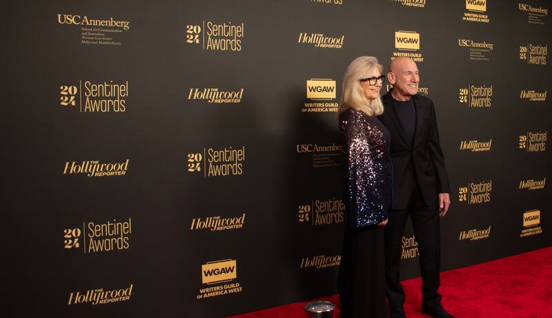 Katie is wearing a purple and blue sequined jacket with black suit pants. Martin is wearing an all black suit.