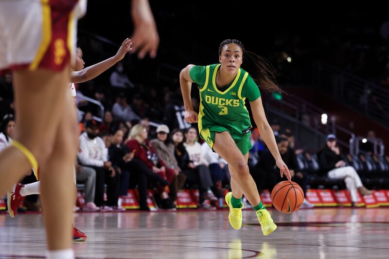 Sophia Bell (3) dribbles a basketball upcourt at Galen Center. She wears a green basketball uniform with yellow accents and sneakers.