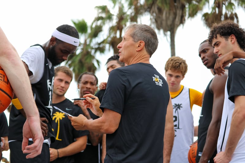 Eric Musselman stands in profile as he coaches a huddle of USC basketball players surrounding him.