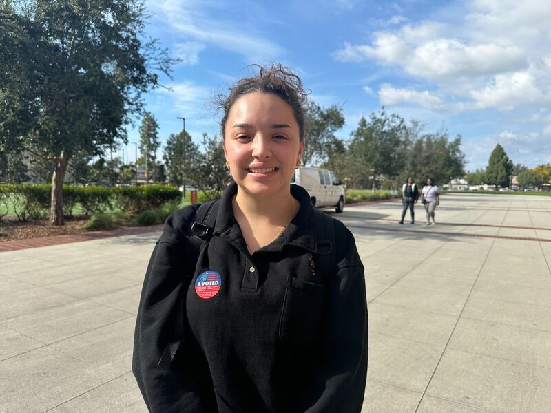 Urquiza stands in front of a lawn, wearing an "I Voted" sticker.