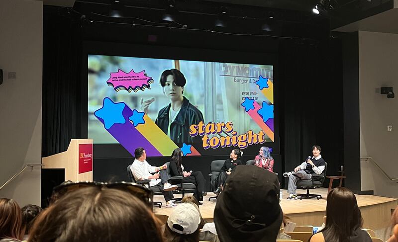 Photo of five people watching a video on stage