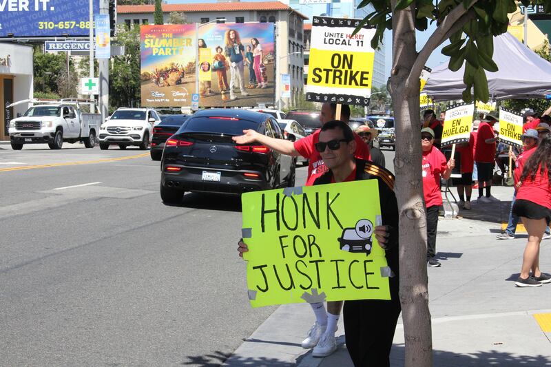 Marcus Molina holds up a “Honk For Justice” sign as cars zoom by at the One Hotel in West Hollywood on July 21st, 2023.